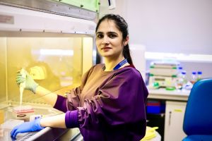 PhD Scholar Nazia Akram stands in a lab in a lab coat.